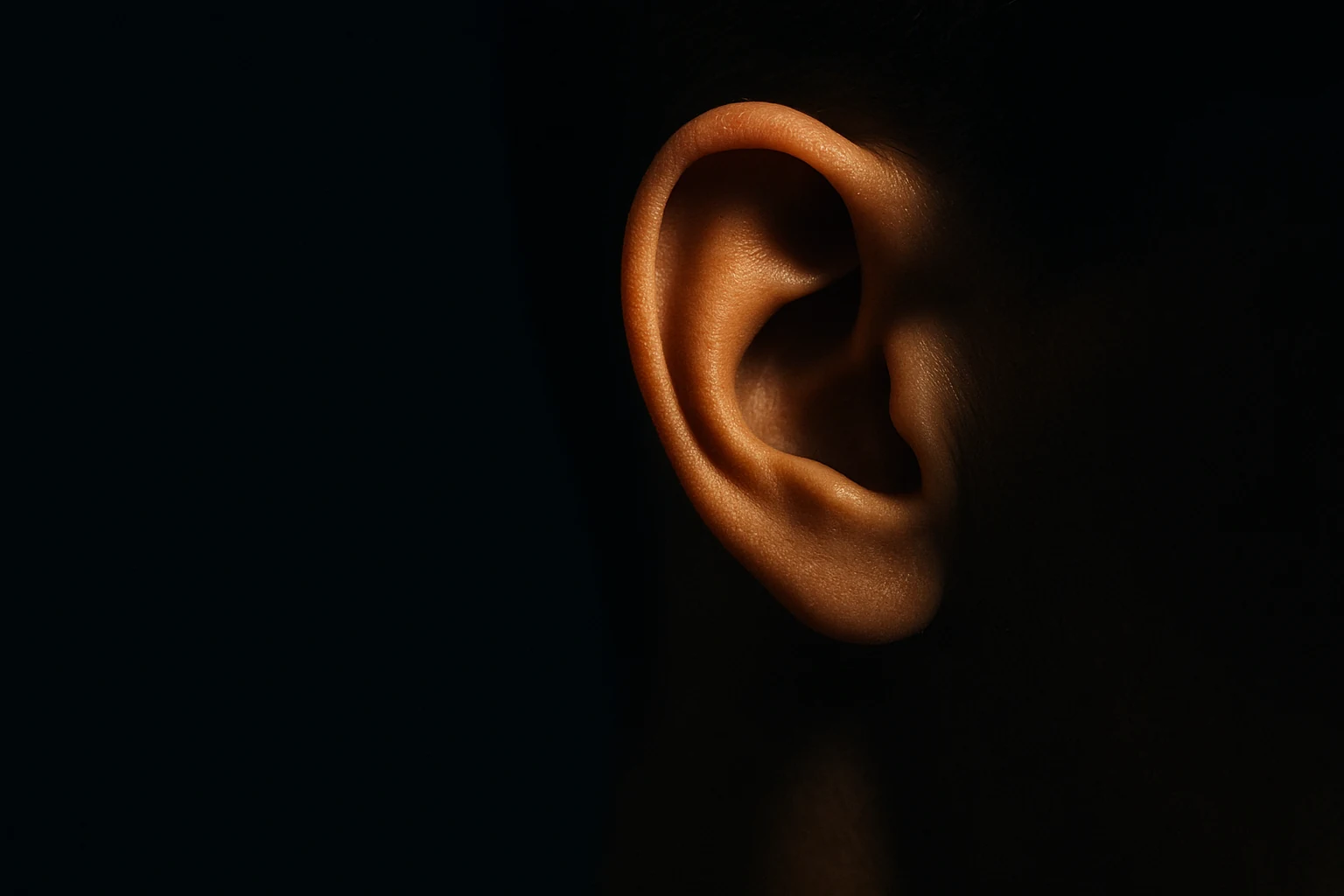 A single human ear in profile, lit warm against deep black, catching light as if caught mid-hearing.